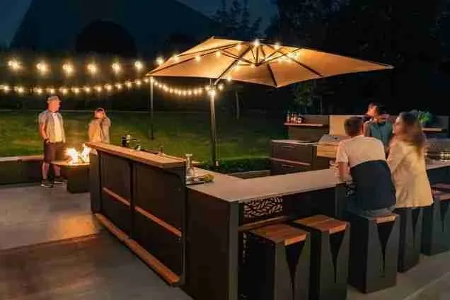 Outdoor kitchen with bar seating and standing bar with fairy lights in the evening