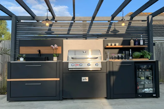 Outdoor kitchen on decking with gas bbq, sink and fridge and bin cabinets