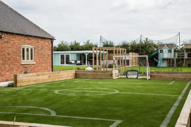 football pitch overlooking outdoor kitchen under roof of summerhouse in Warwickshire garden