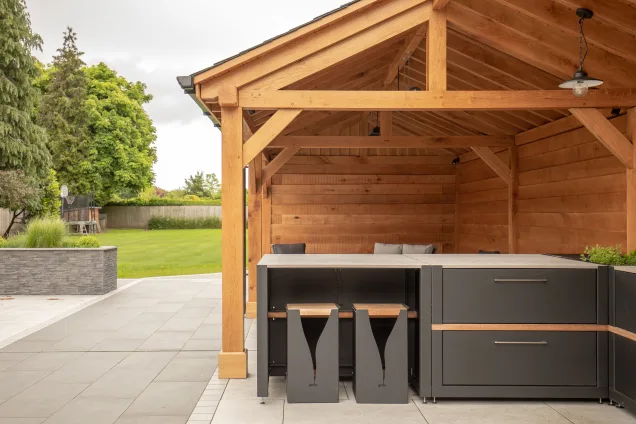 Outdoor kitchen in Cheshire under wooden pergola on patio with stools