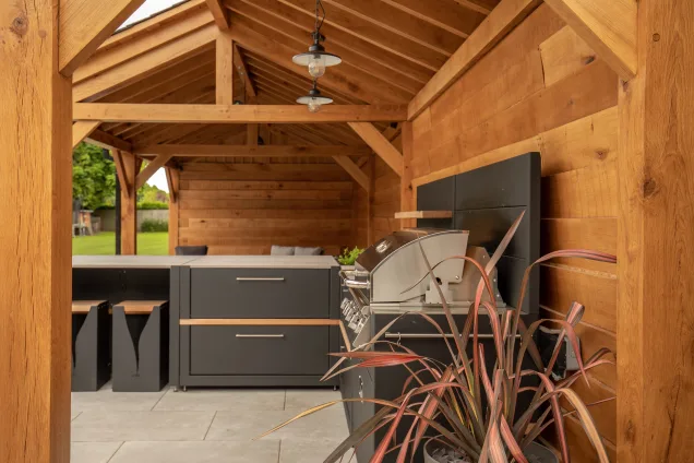 Outdoor kitchen in Cheshire under wooden pergola on patio with stools gas bbq and storage cabinet