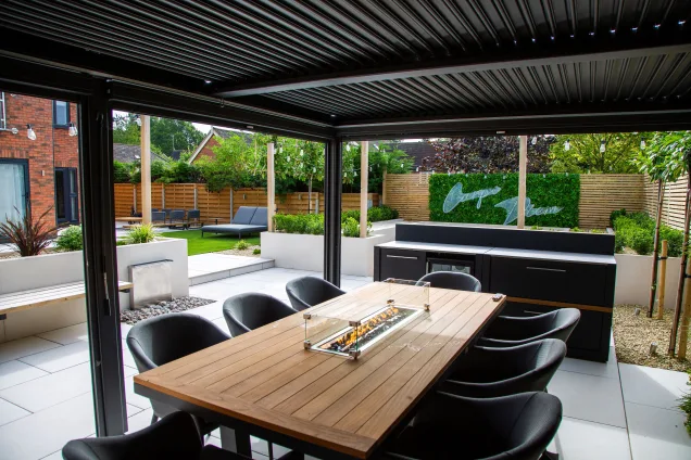 Outdoor kitchen in Leicestershire under pergola with dining table with bar cabinets with fridge and storage