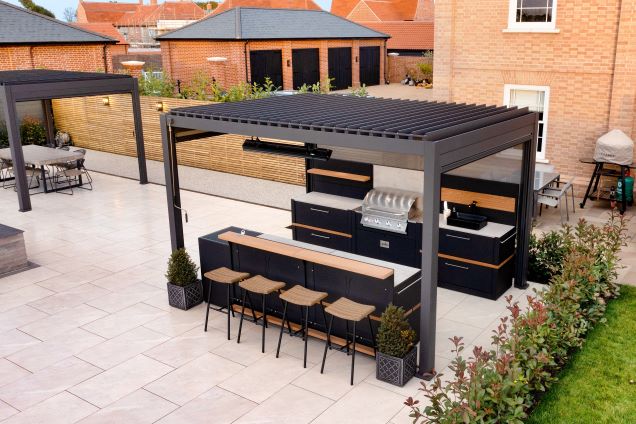 outdoor kitchen under pergola with gas bbq and sink and bar table and stools