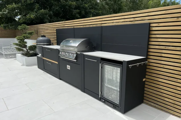 Outdoor kitchen with gas bbq and storage and fridge and bin against wooden fence
