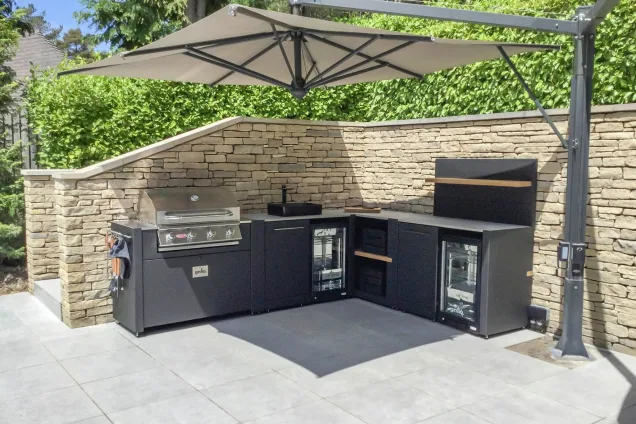Outdoor kitchen under canopy on patio with gas bbq, sink, two fridges and storage space