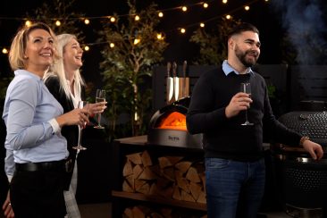 people socialising in outdoor kitchen with a pizza oven on worktop