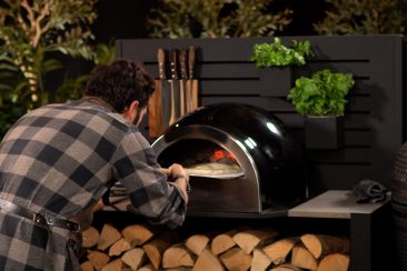 person putting pizza into pizza oven on pizza peel