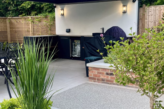 outdoor kitchen next to planters, under a pergola and on a large patio
