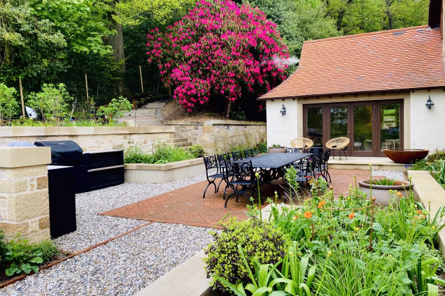 outdoor kitchen with gas and charcoal bbqs in mature garden with large outdoor table and chairs