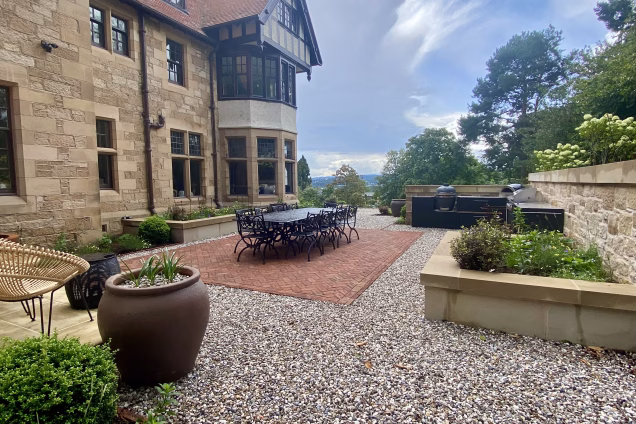 large garden next to big house with outdoor table and chairs and outdoor kitchen