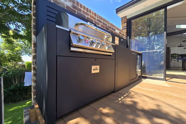 Low level photo looking along an outdoor kitchen into the open-plan kitchen-diner of a residential house in Naremburn NSW. The indoor living space leads seamlessly into the outdoor living space.