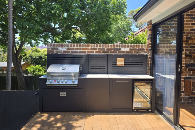 A tidy-looking straight run of outdoor kitchen with a gas grill, fridge, and matching black slatted feature walls on a deck in Naremburn NSW