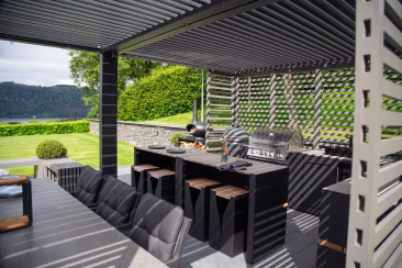 outdoor kitchen with bbqs and bar seating and sink under pergola with slatted walls