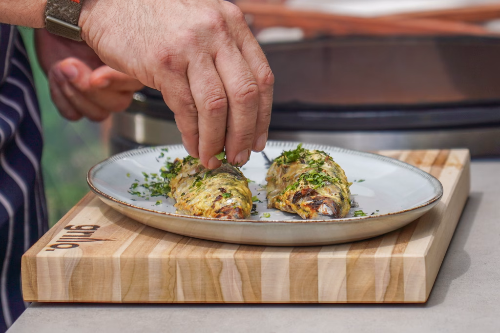 A chef's hand sprinkles minced coriander and mint over grilled mackerel
