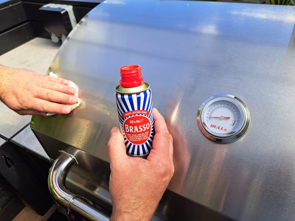 Photo showing a man's hands using Brasso metal polish to carefully refresh a Bull gas grill, taking care to rub with the grain