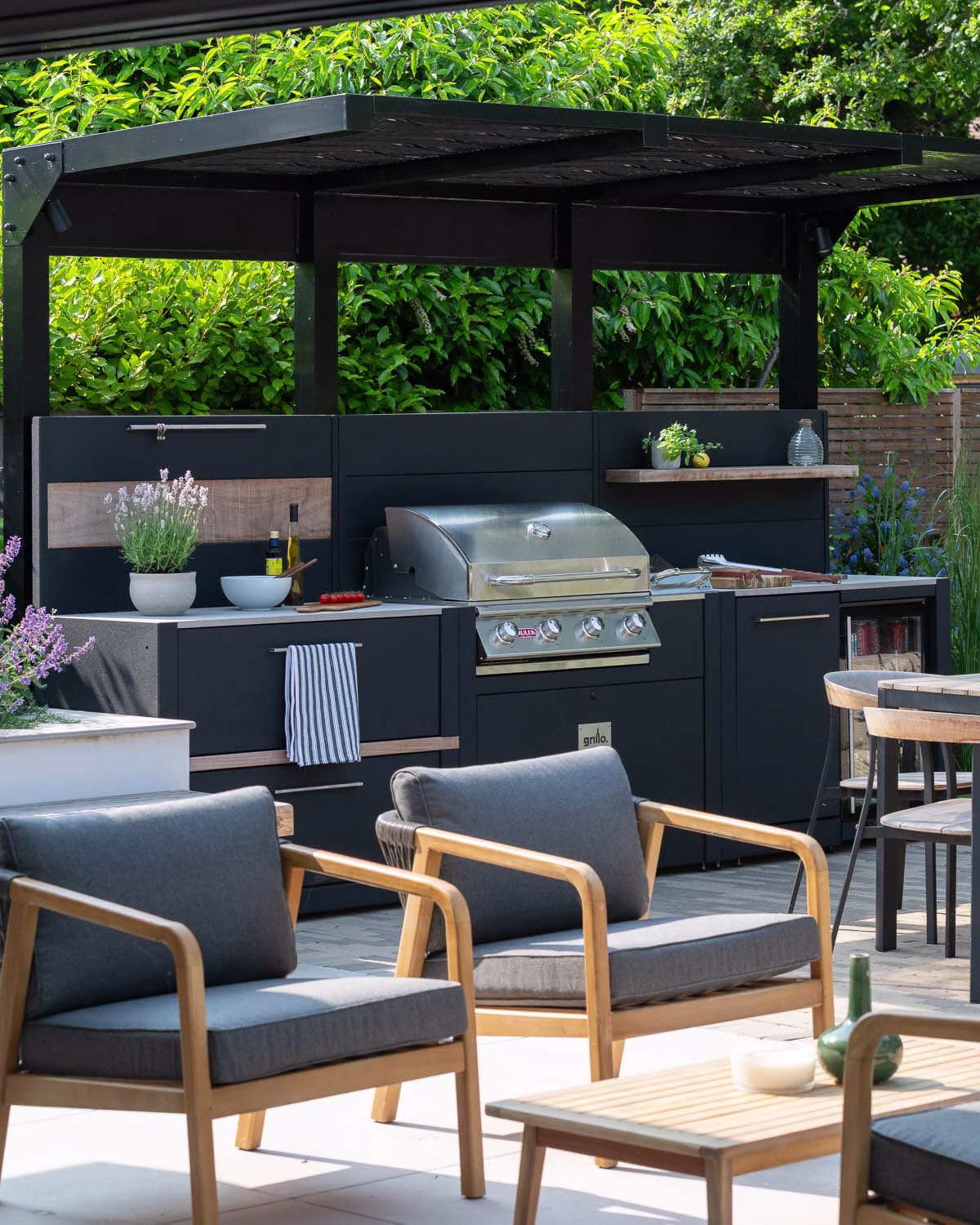 outdoor kitchen under metal covering with bbq and fridge, next to seating area