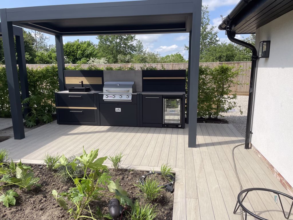 outdoor kitchen on decking under pergola with bull gas grill station, drinks fridge and bin and storage